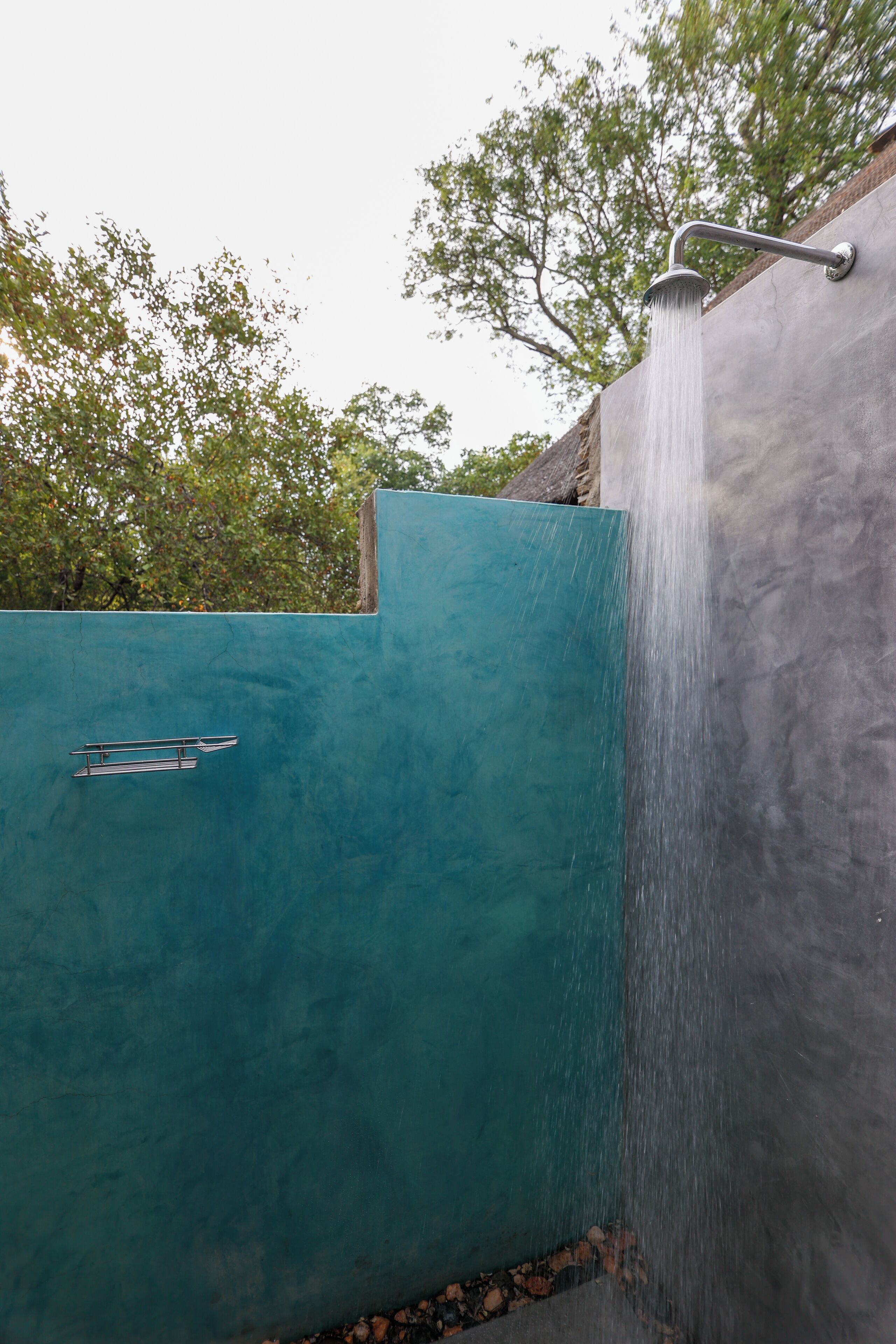 Eine Dusche mit Wasserfallarmatur vor einer türkisblauen Wand, mit einer steinernen Auflage am Boden.