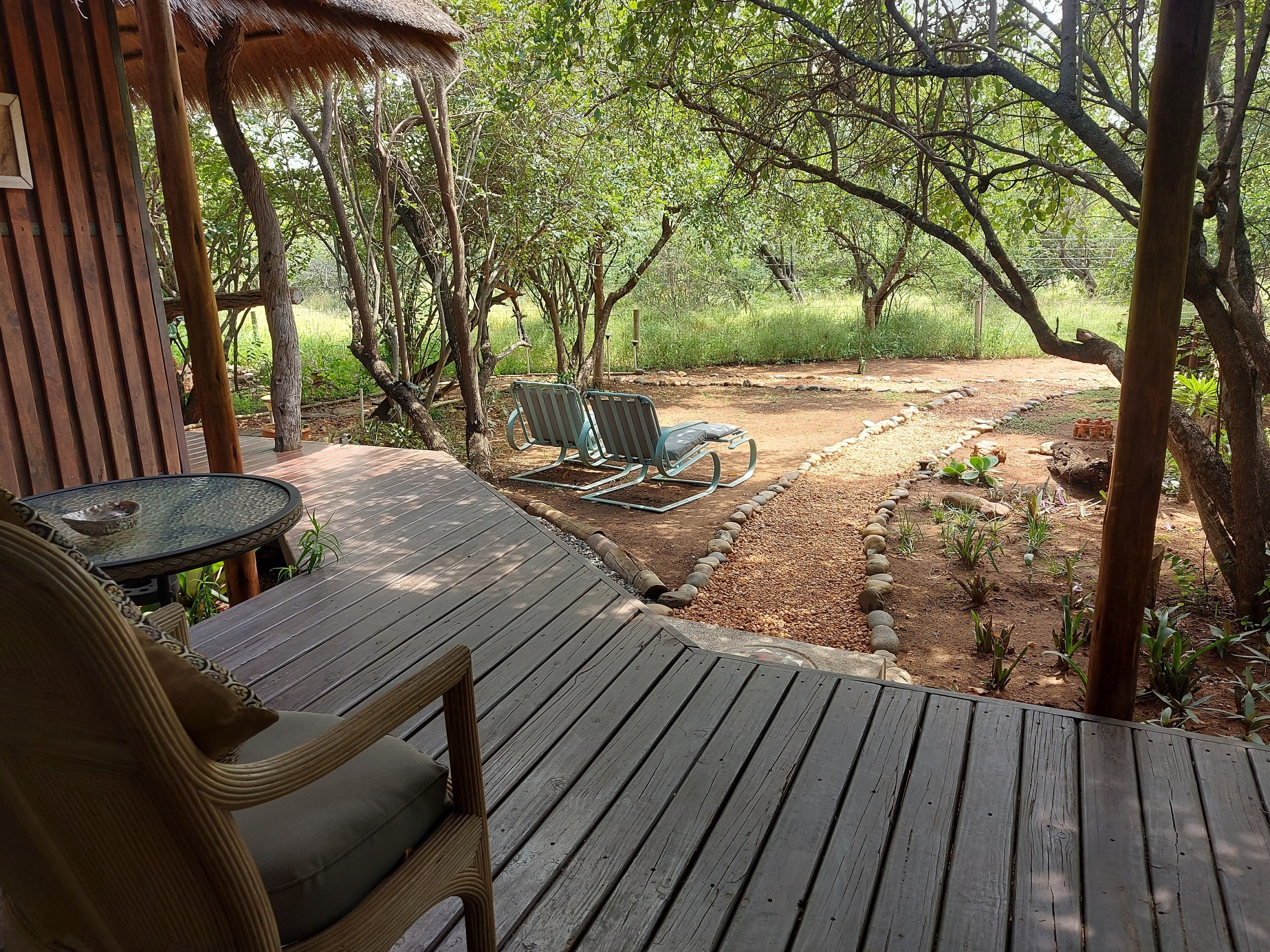 A wooden deck with a table and chairs, surrounded by trees and a garden area.