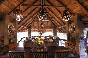 A thatched-roof dining area with wooden furniture and hanging spherical light fixtures. - Call of the Wild Lodge (Hoedspruit)
