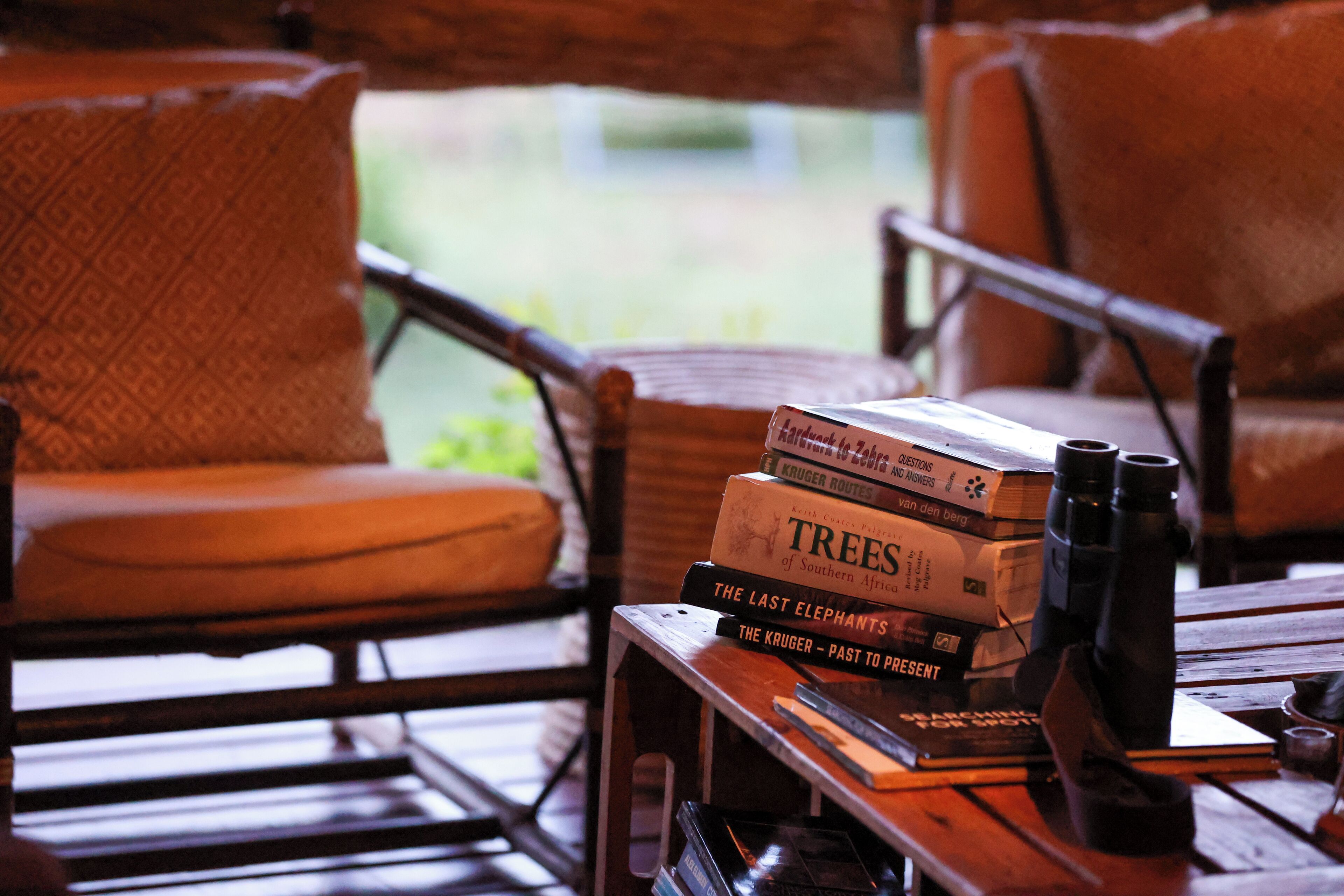 A wooden table with books and binoculars, surrounded by wicker chairs.