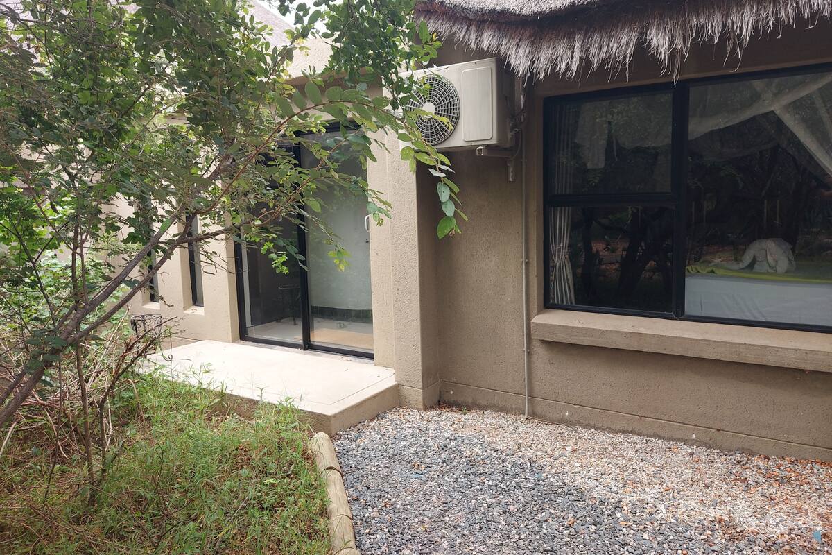 A building with a thatched roof, a window with a view of a room, and an air conditioning unit mounted on the wall.