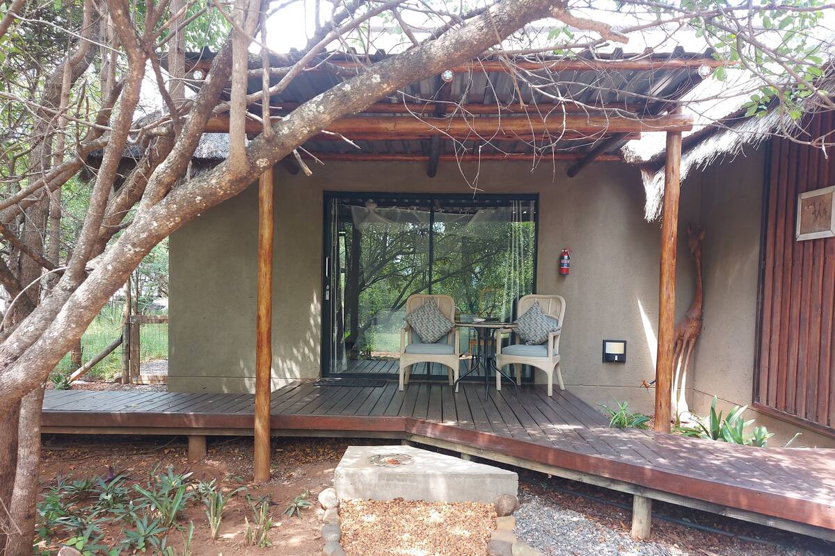 A covered outdoor seating area with two chairs and a table, surrounded by trees and a wooden deck.