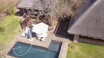 A residential property with a swimming pool, patio furniture, and a thatched-roof structure.