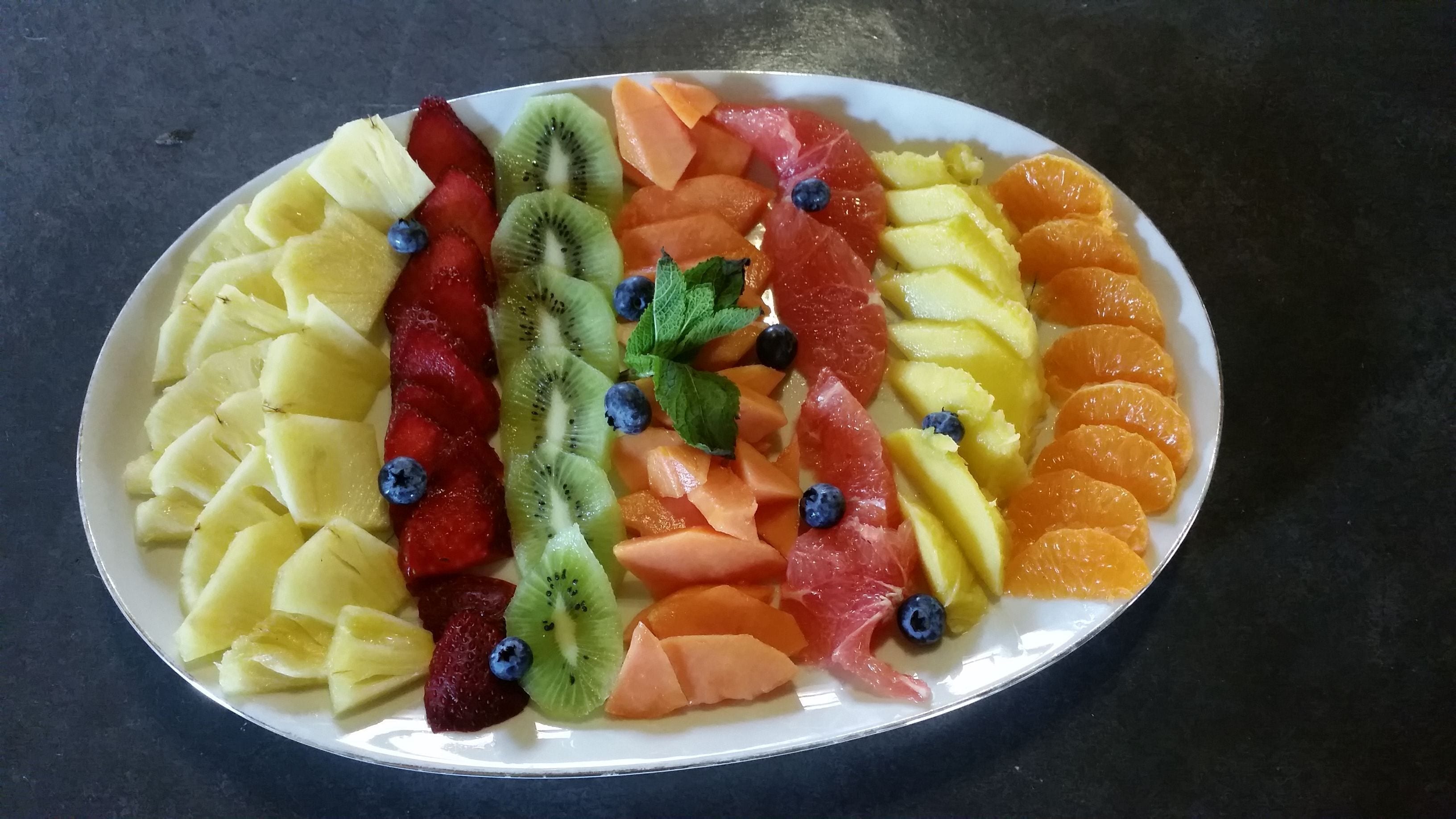 A plate of assorted fruits including pineapple, strawberries, kiwi, cantaloupe, and oranges.