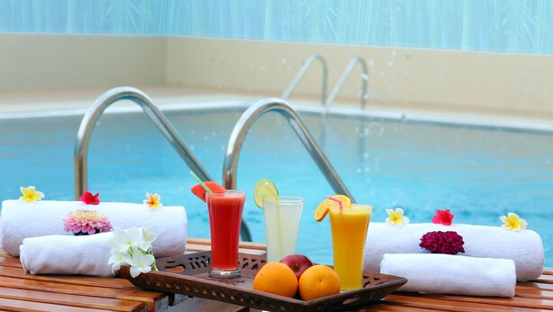 Escena junto a la piscina con toallas, fruta y bebidas.