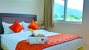 Una cama bien hecha con colcha roja, almohadas blancas y un arreglo decorativo de toallas y flores.