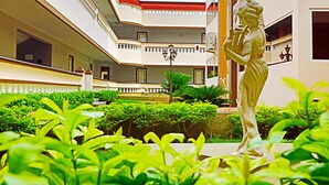 Un patio con una estatua, abundante vegetación y un edificio con balcones y un techo rojo.