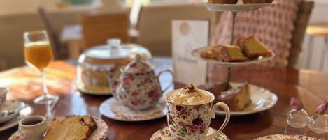 Una mesa dispuesta para una ceremonia de té, con tazas de estampado floral, teteras y una bandeja escalonada de pasteles.