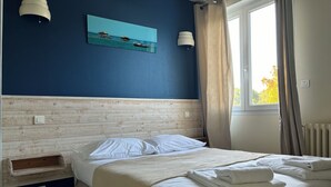 Une chambre à coucher avec une tête de lit en bois, un lit recouvert de draps blancs, un tableau représentant une scène de plage et une fenêtre avec des rideaux.