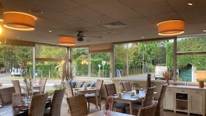 Un restaurant doté de meubles en osier, de grandes fenêtres et de luminaires suspendus.