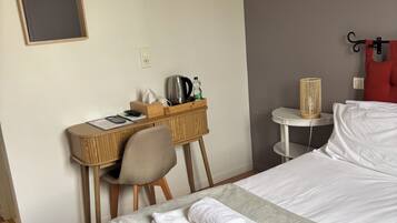 Habitación de hotel con cama, escritorio, silla, mesita de noche y lámpara de pared.