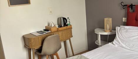 Ett hotellrum med en säng, ett skrivbord, en stol, ett sängbord och en vägglampa.
