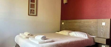 A neatly made bed with white linens and rolled towels, a wooden headboard, and two wall-mounted lamps.
