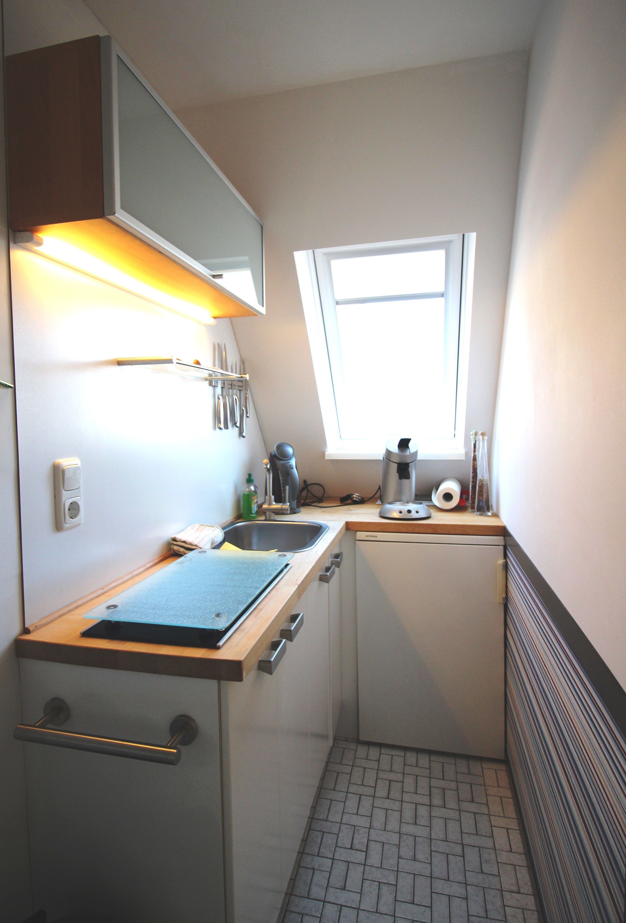 A compact kitchen with a window, a sink, a coffee maker, and a small refrigerator.