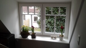 A window with a view of a house and trees. There are three flower pots on the windowsill. - Hus Mattgoot (St. Peter-Ording)