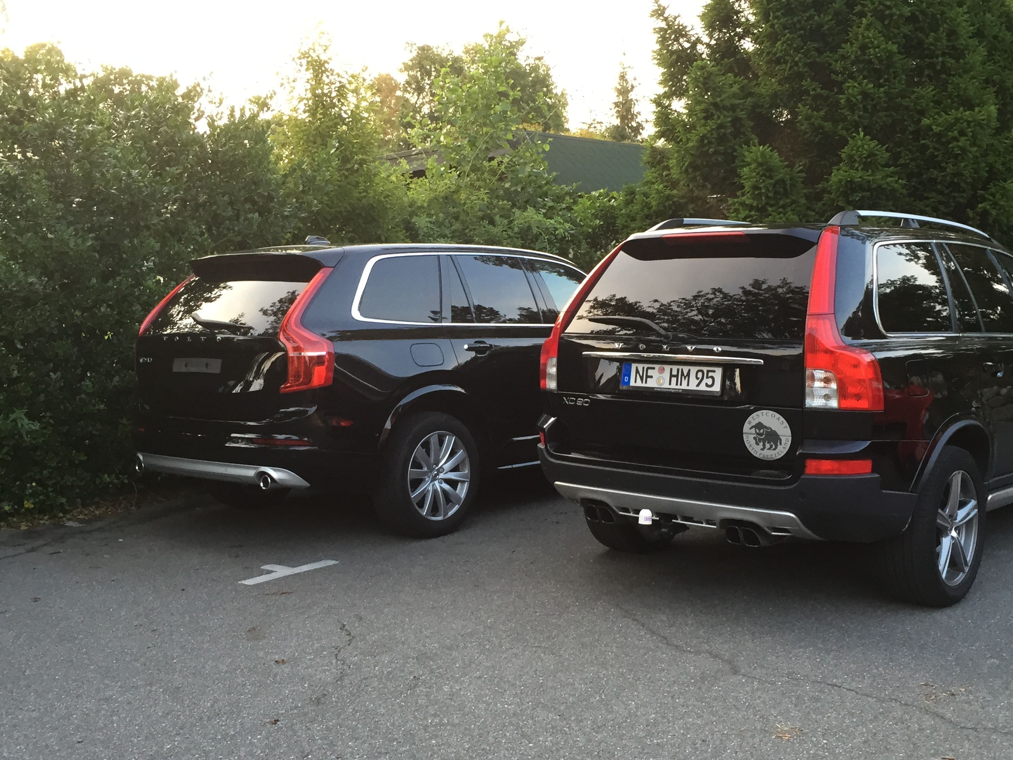 Two black SUVs parked side by side on a paved road with trees in the background.
