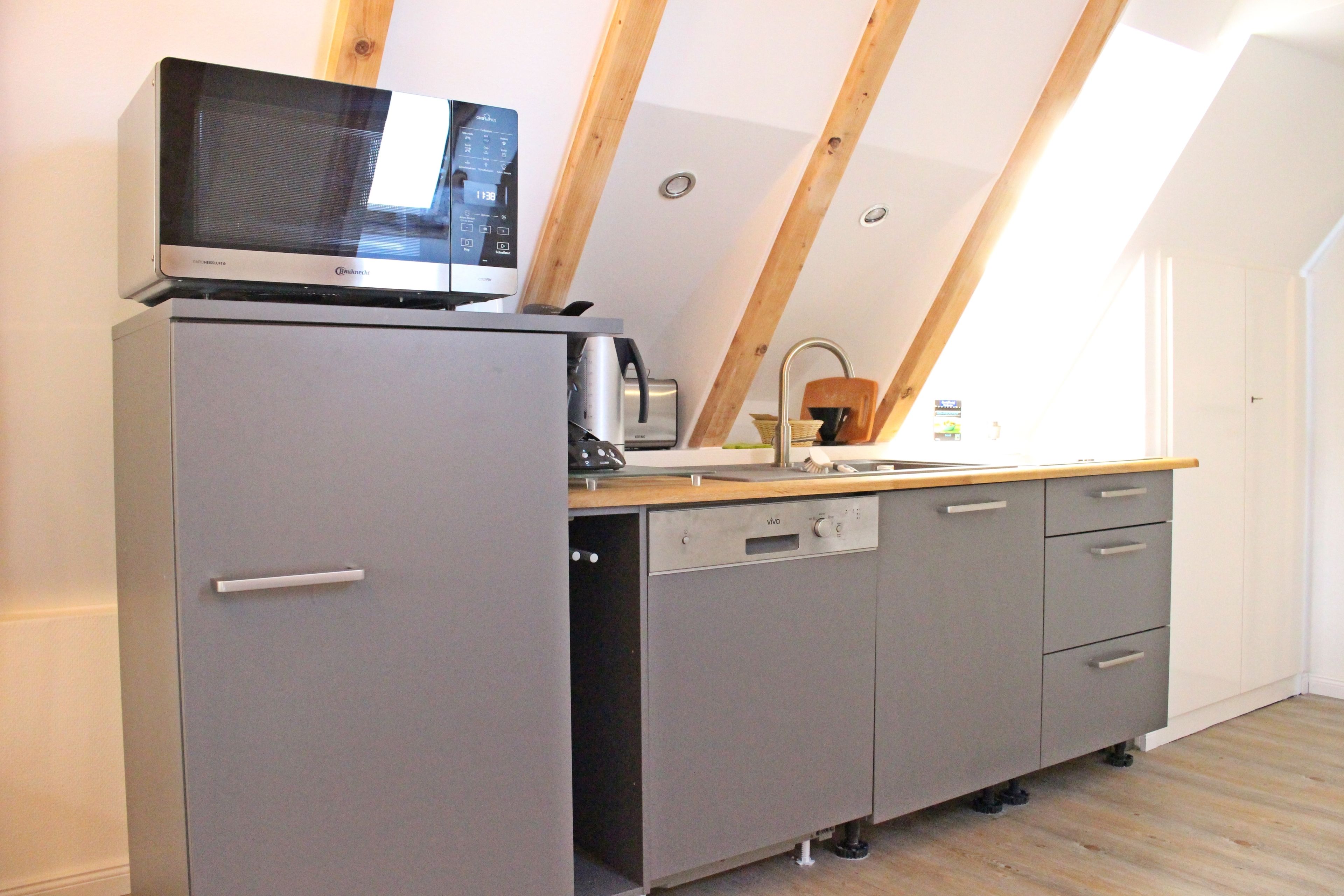 A compact kitchen with a built-in microwave, a dishwasher, and a wooden countertop.