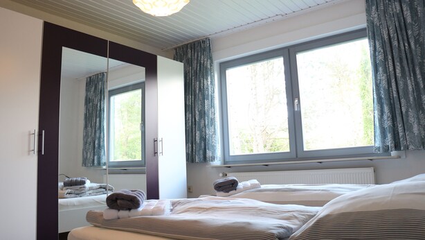 Ein Schlafzimmer mit großem Spiegel, zwei Betten, einem Heizkörper und einem Fenster mit Vorhängen.