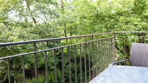 Ein Balkon mit Metallgeländer und Korbmöbeln, umgeben von dichtem Grün.