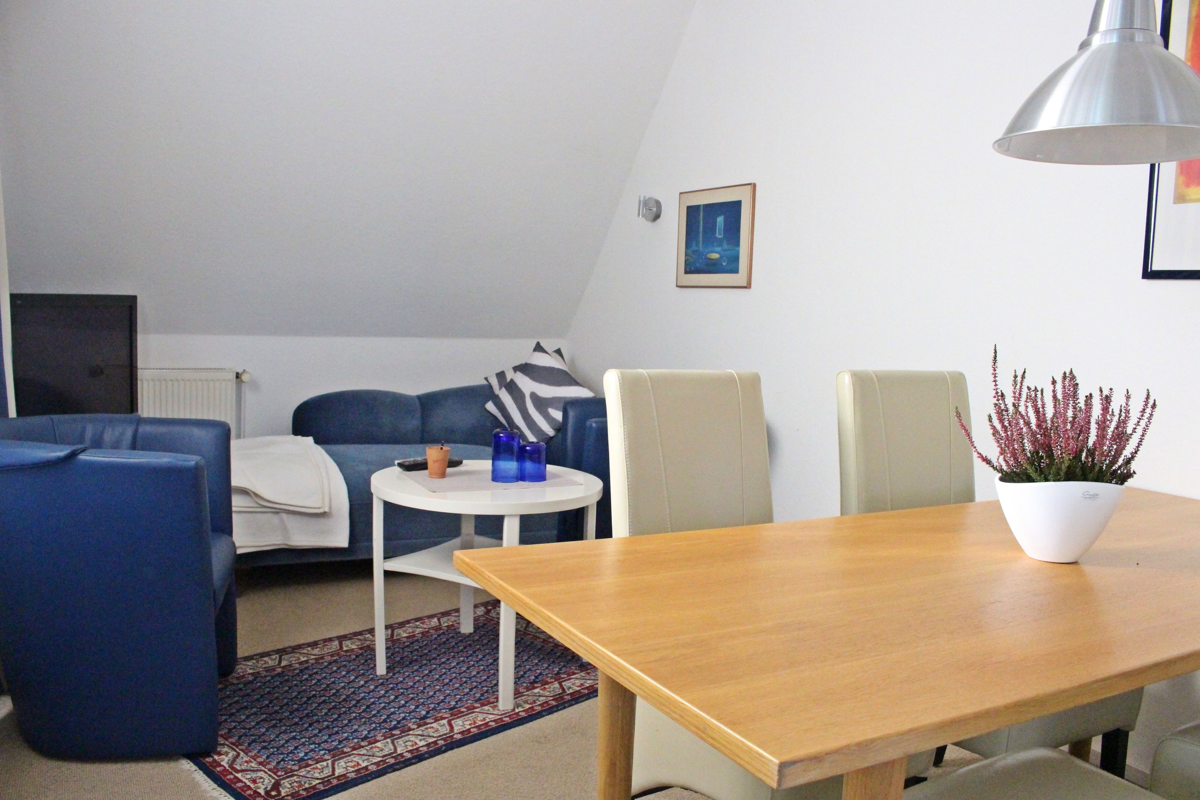 A modern living room with a sofa, a small round table with a lamp, and a wooden dining table.