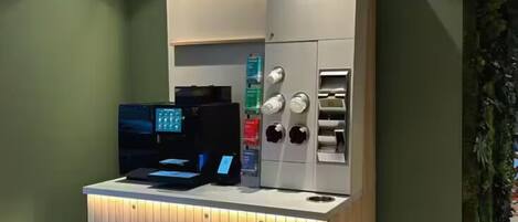 A Starbucks coffee machine with a digital display and a cash register, set against a green wall with a wooden counter.