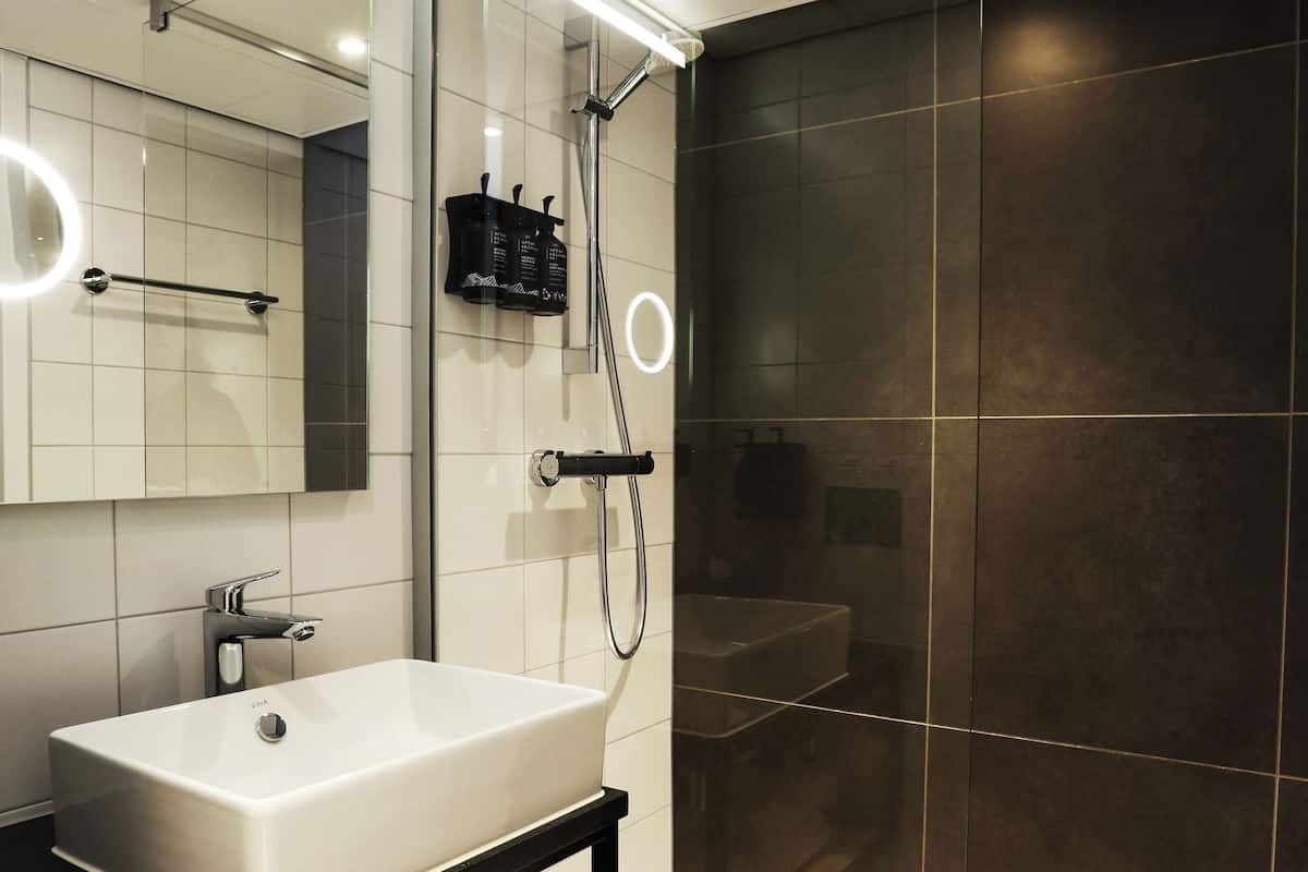 A modern bathroom with a white sink, dark tiled shower, and a mirror with lights.