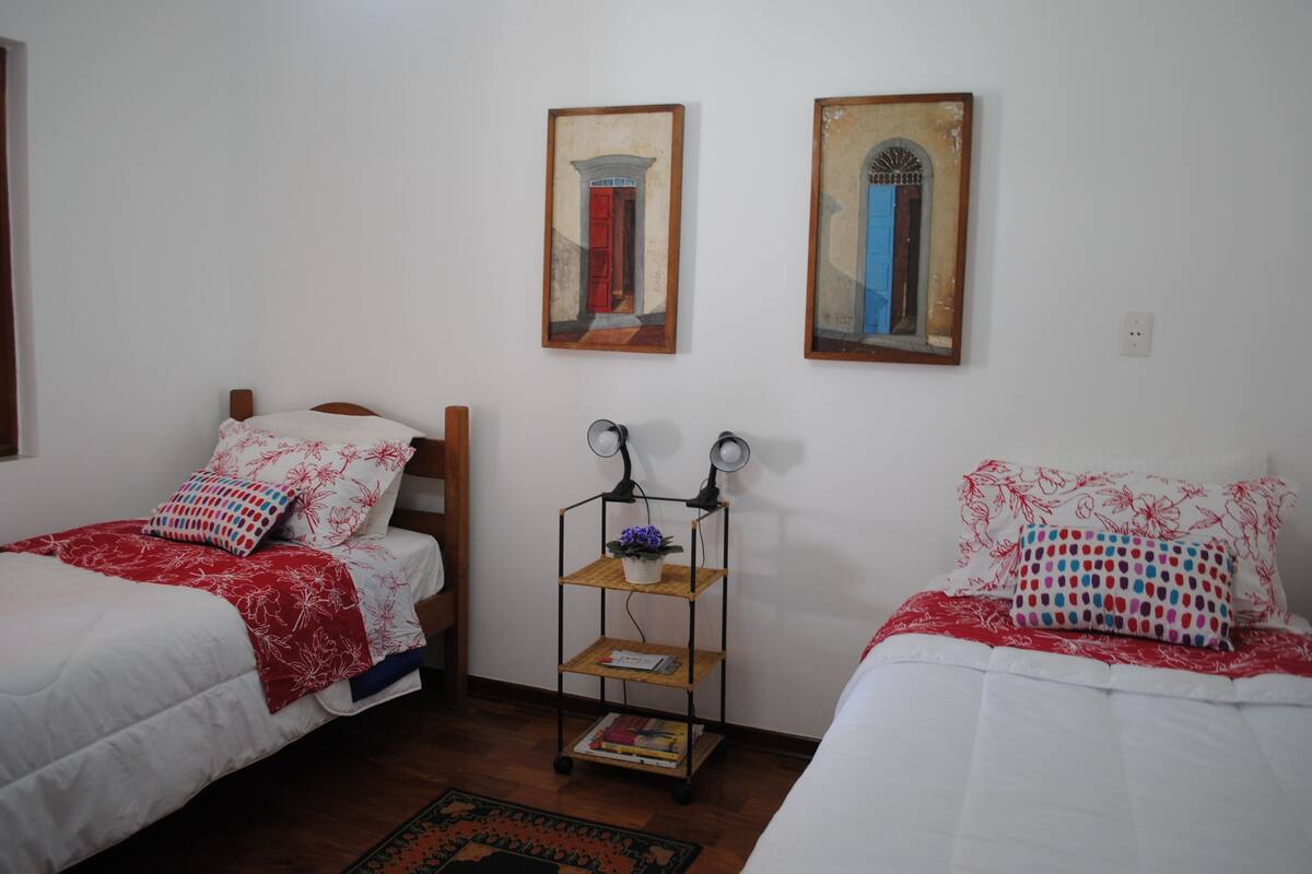 Une chambre avec deux lits simples, une table de chevet avec une lampe et une petite étagère.