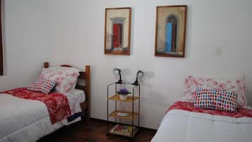 Quarto com duas camas de solteiro, uma mesa de cabeceira com luminária e um pequeno aparador.