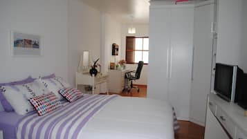 Um quarto com cama, escrivaninha, cadeira, televisão e guarda-roupa.