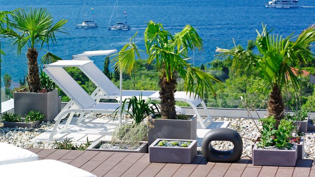 A rooftop terrace with lounge chairs, planters with tropical plants, and a view of the sea with boats. - Lifestyle Hotel Vitar - Adults Only (Bol)