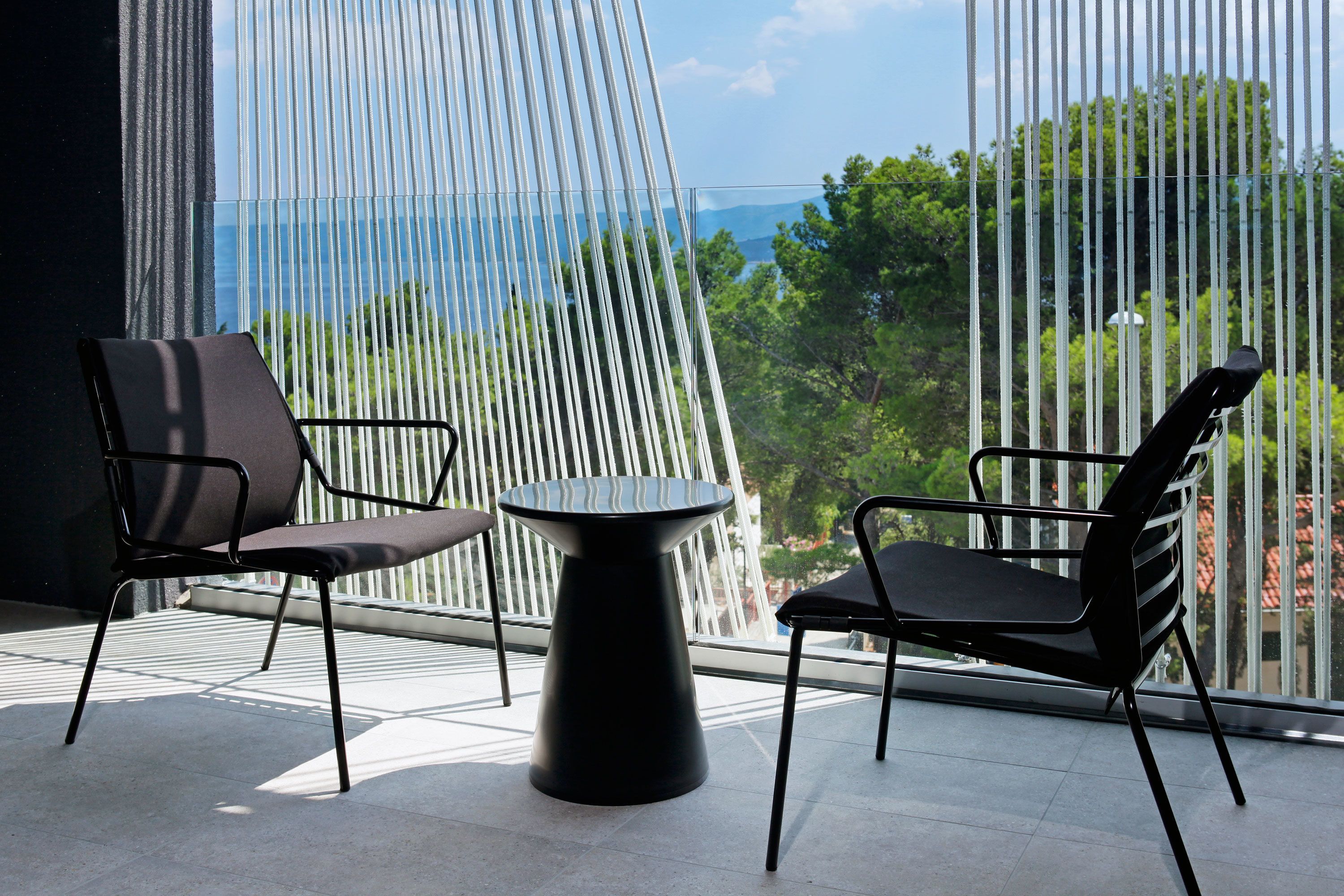A modern outdoor seating area with two chairs and a table, overlooking a scenic view through a patterned window.