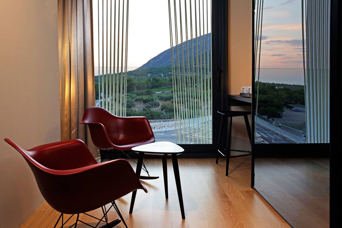A modern room with two red chairs, a small white table, and a view of a mountainous landscape through large windows.