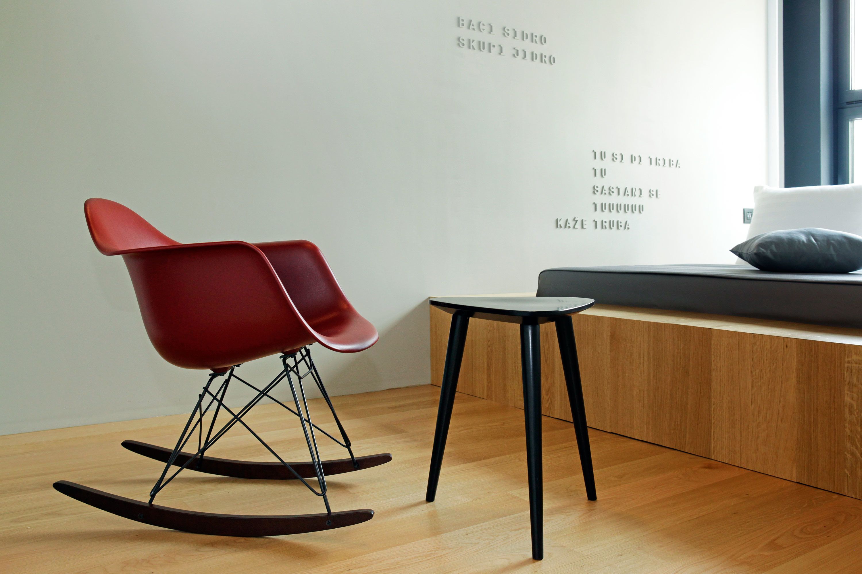 A modern room with a red rocking chair, a small table, and a wall with text.