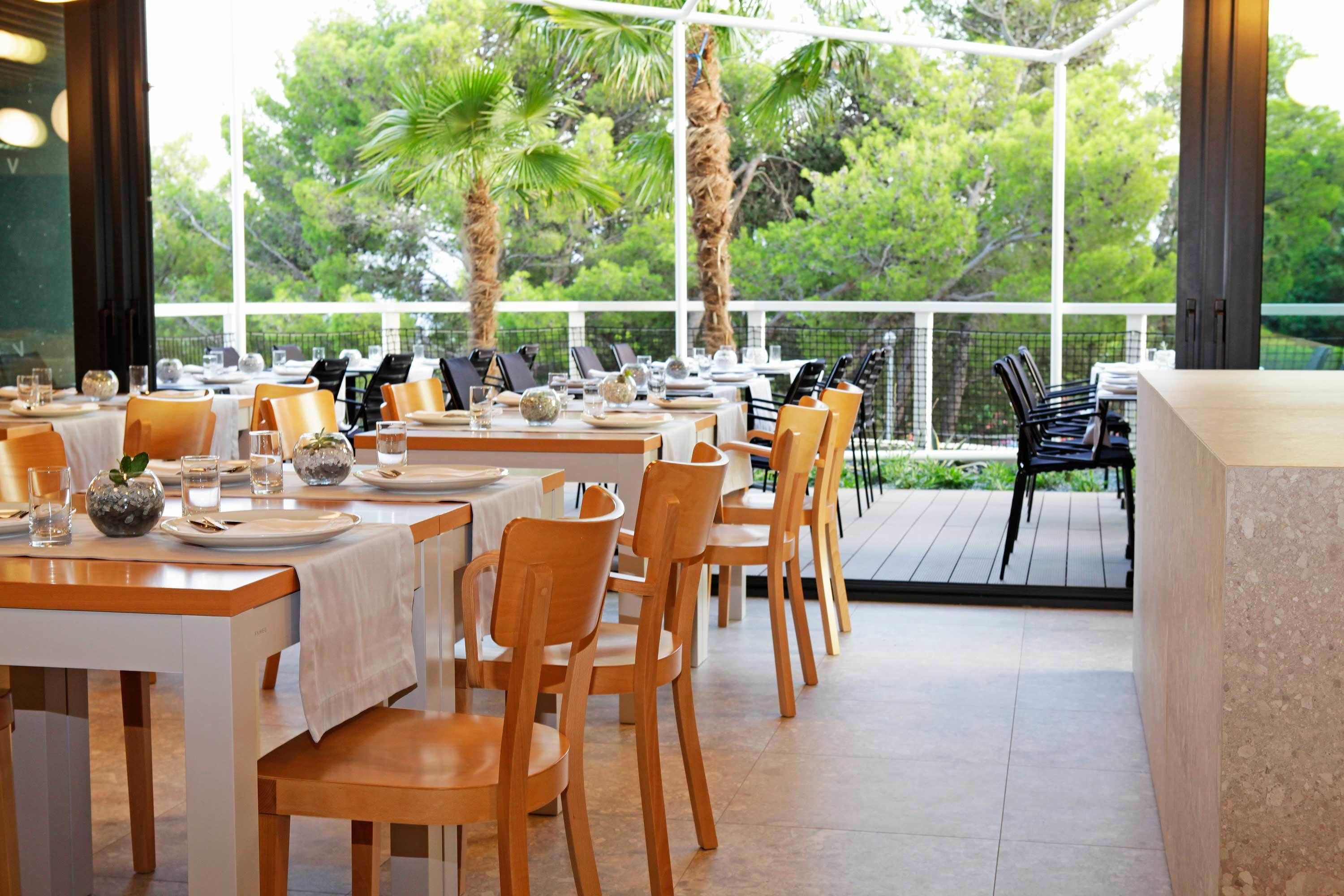 An outdoor dining area with tables set for a meal, surrounded by chairs and palm trees.