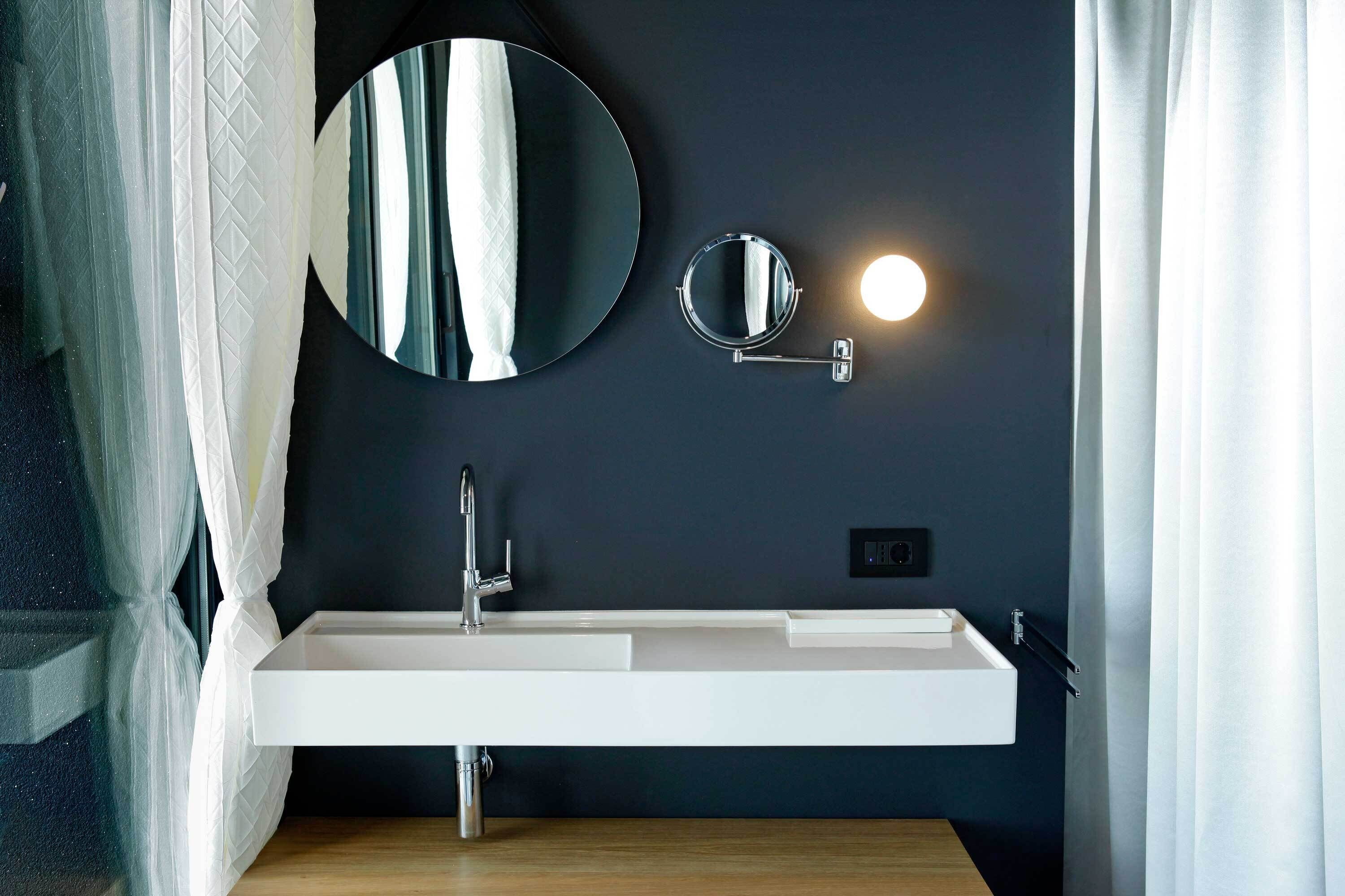 A modern bathroom with a white sink, a round mirror, and a wall-mounted light.