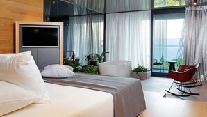 A modern bedroom with a large bed, a TV mounted on the wall, a balcony with a view of the sea, and a red rocking chair. - Lifestyle Hotel Vitar - Adults Only (Bol)
