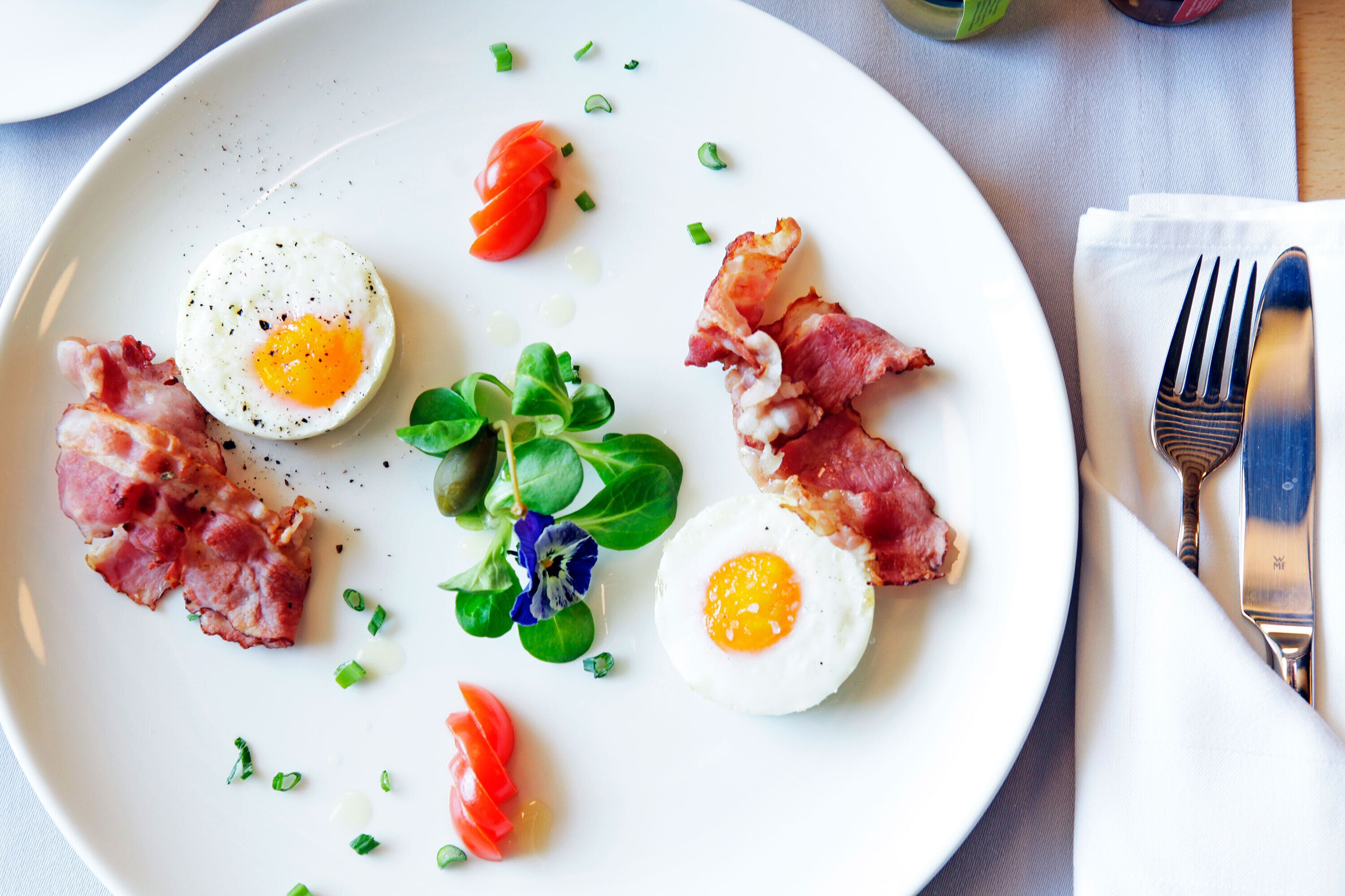 A plate with eggs, bacon, tomatoes, and greens.