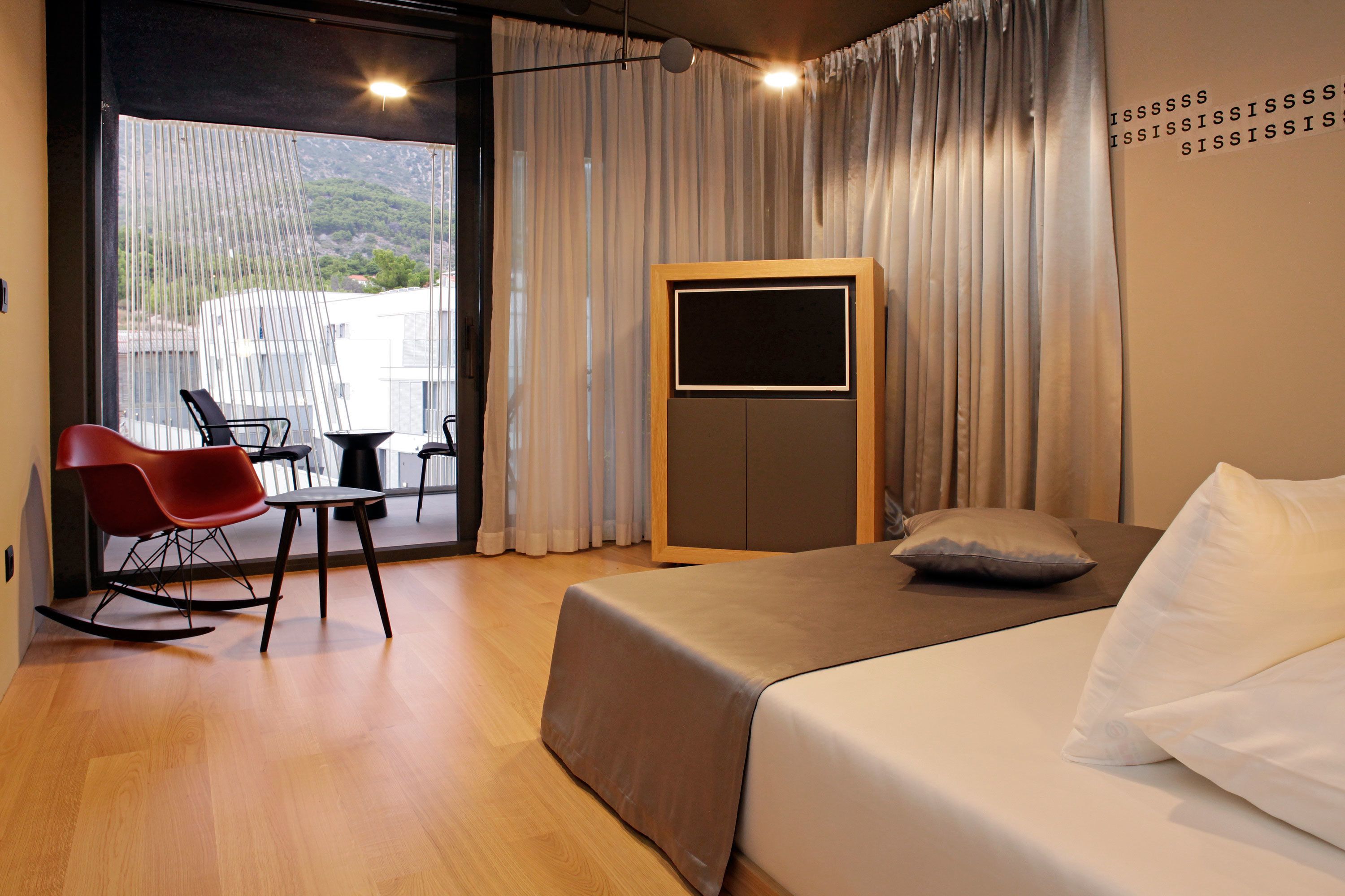 A modern hotel room with a bed, a desk, and a rocking chair.