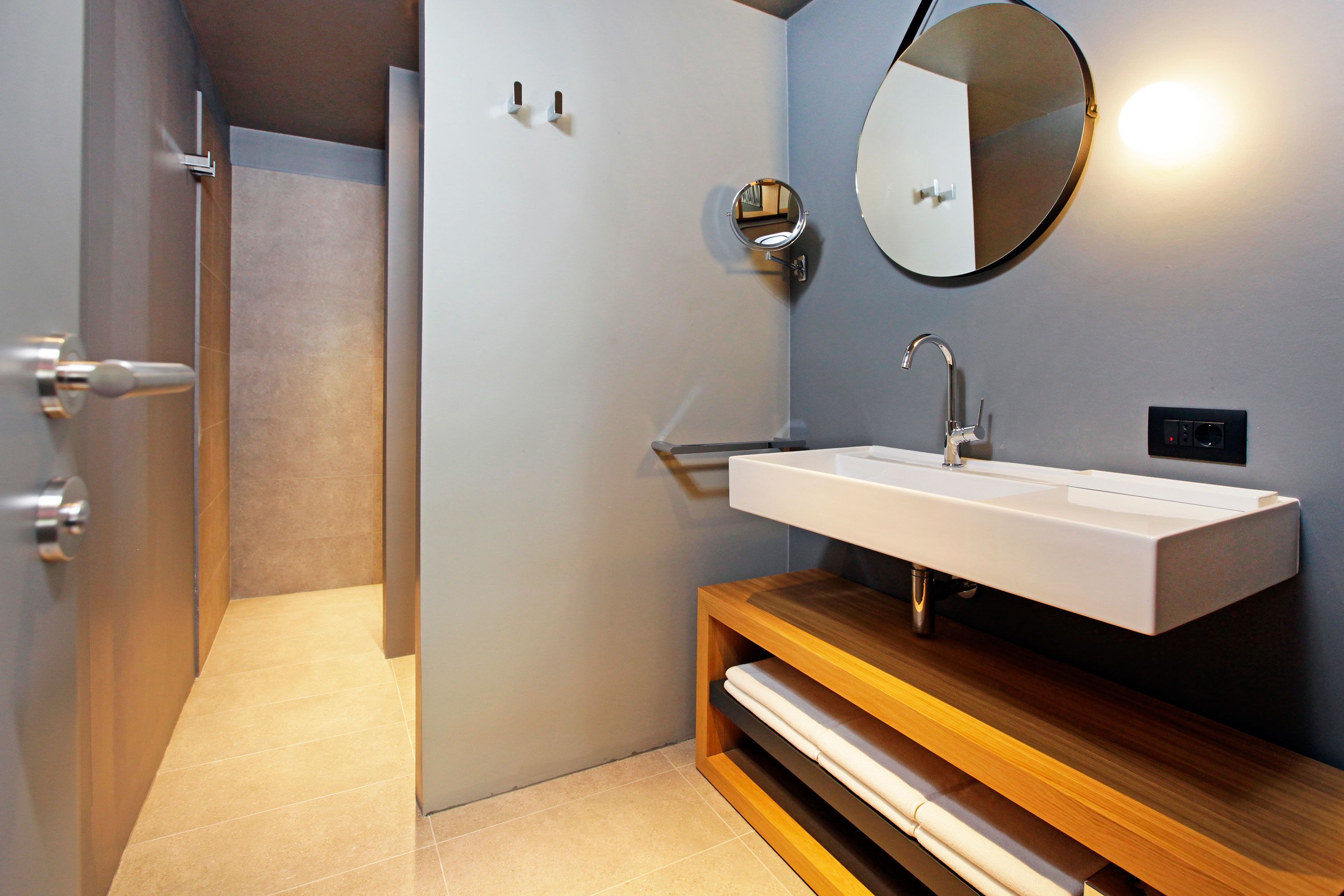 A modern bathroom with a white sink, wooden vanity, and a round mirror.