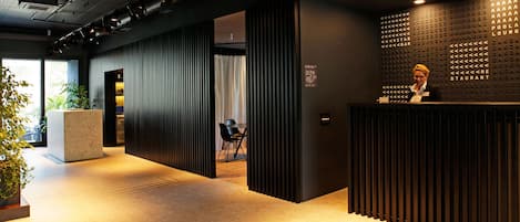 A modern reception area with a dark wood reception desk, a potted plant, and a seating area with a chair and table.
