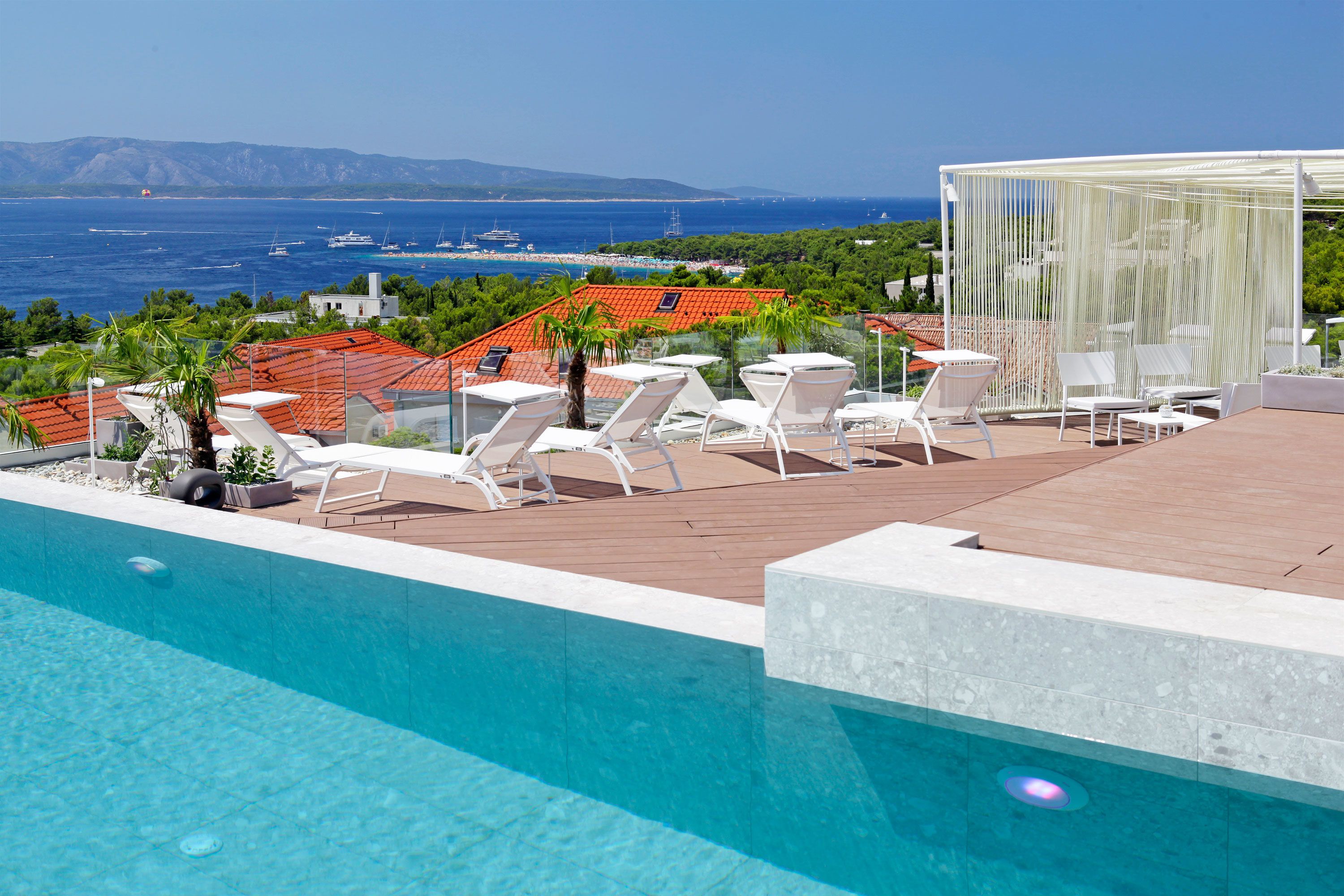 A rooftop pool with lounge chairs, a view of the sea, and a distant beach.