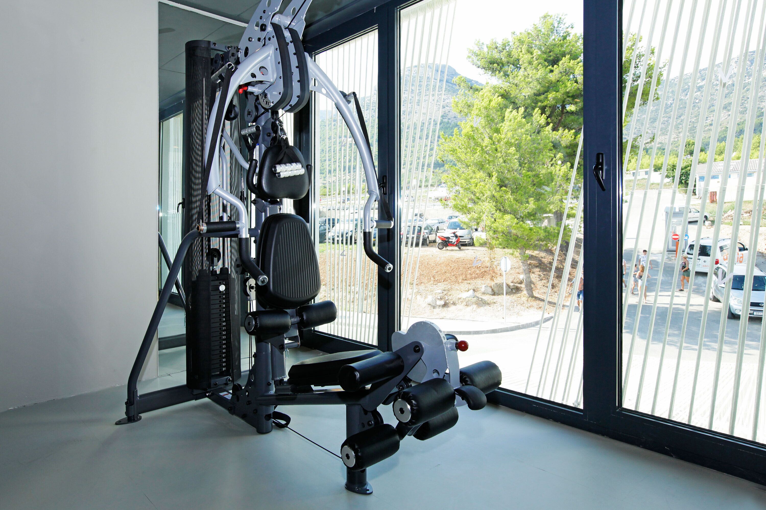 Une salle de sport dotée d’une grande fenêtre, d’une machine de musculation et offrant une vue sur un parking et des arbres à l’extérieur.