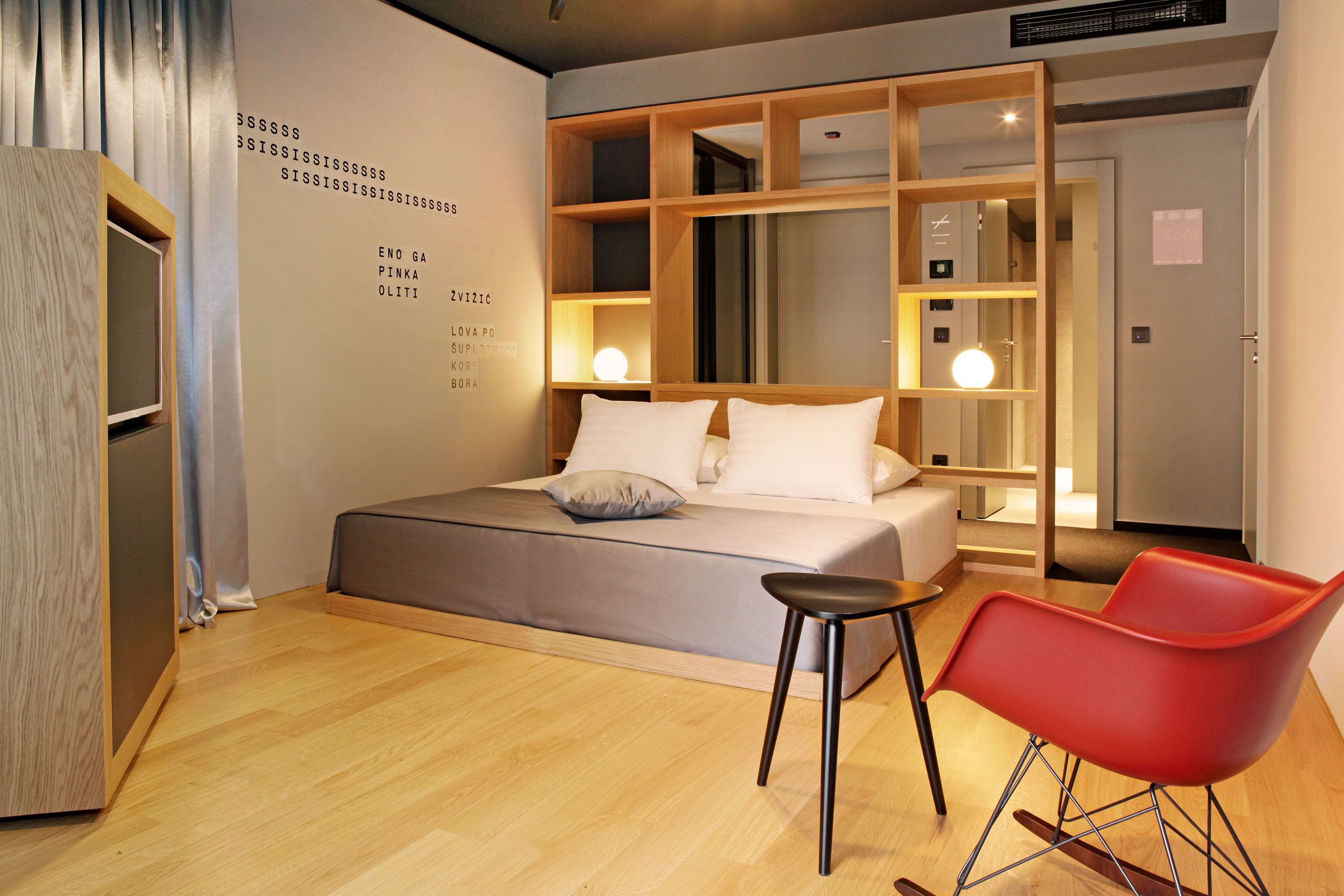 Un dormitorio moderno con una cama grande, una silla roja y un estante de madera.