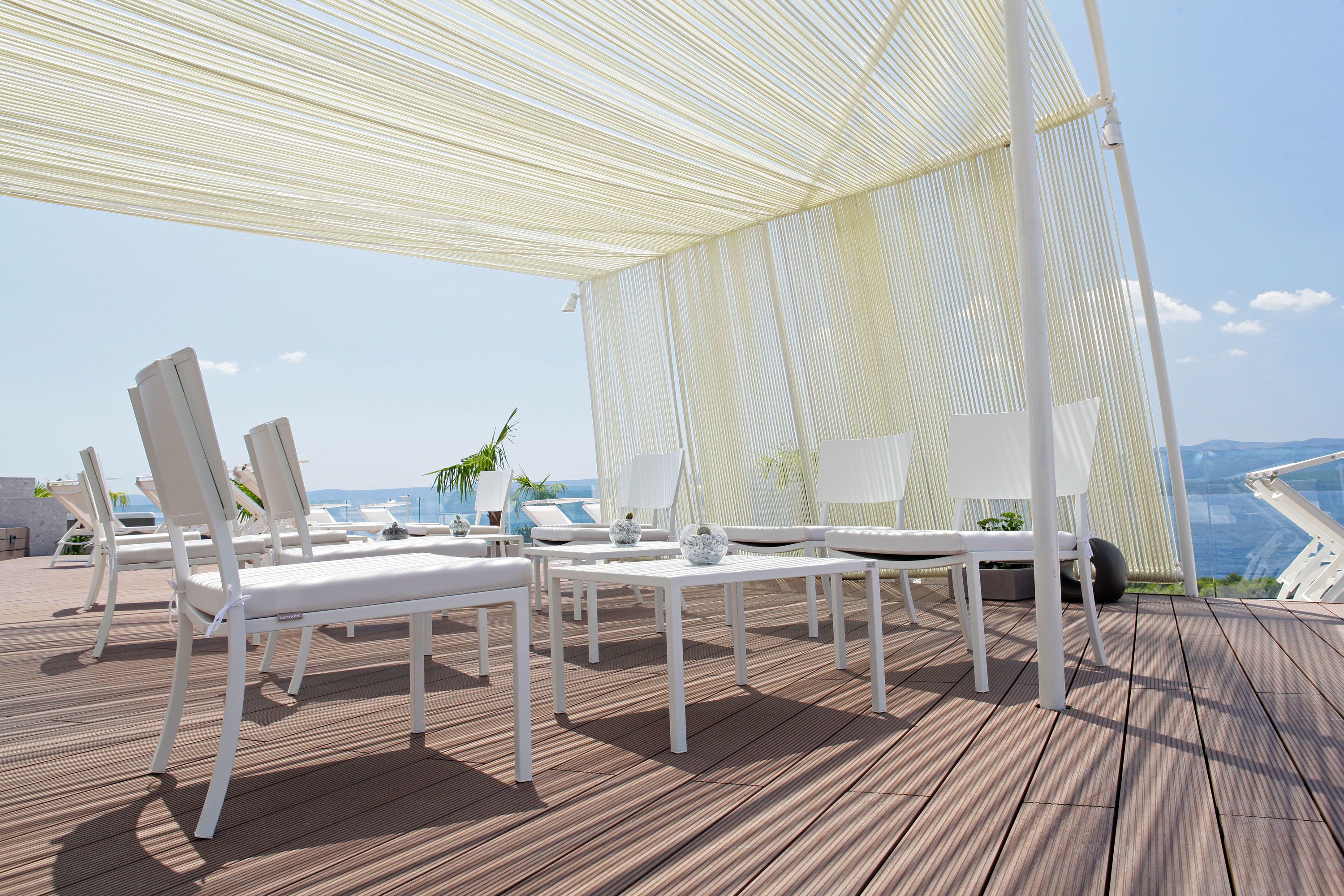 Un área de estar al aire libre con techo, muebles blancos y vista al océano.