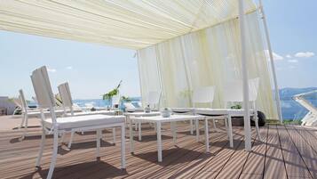 Un área de estar al aire libre con techo, muebles blancos y vista al océano.