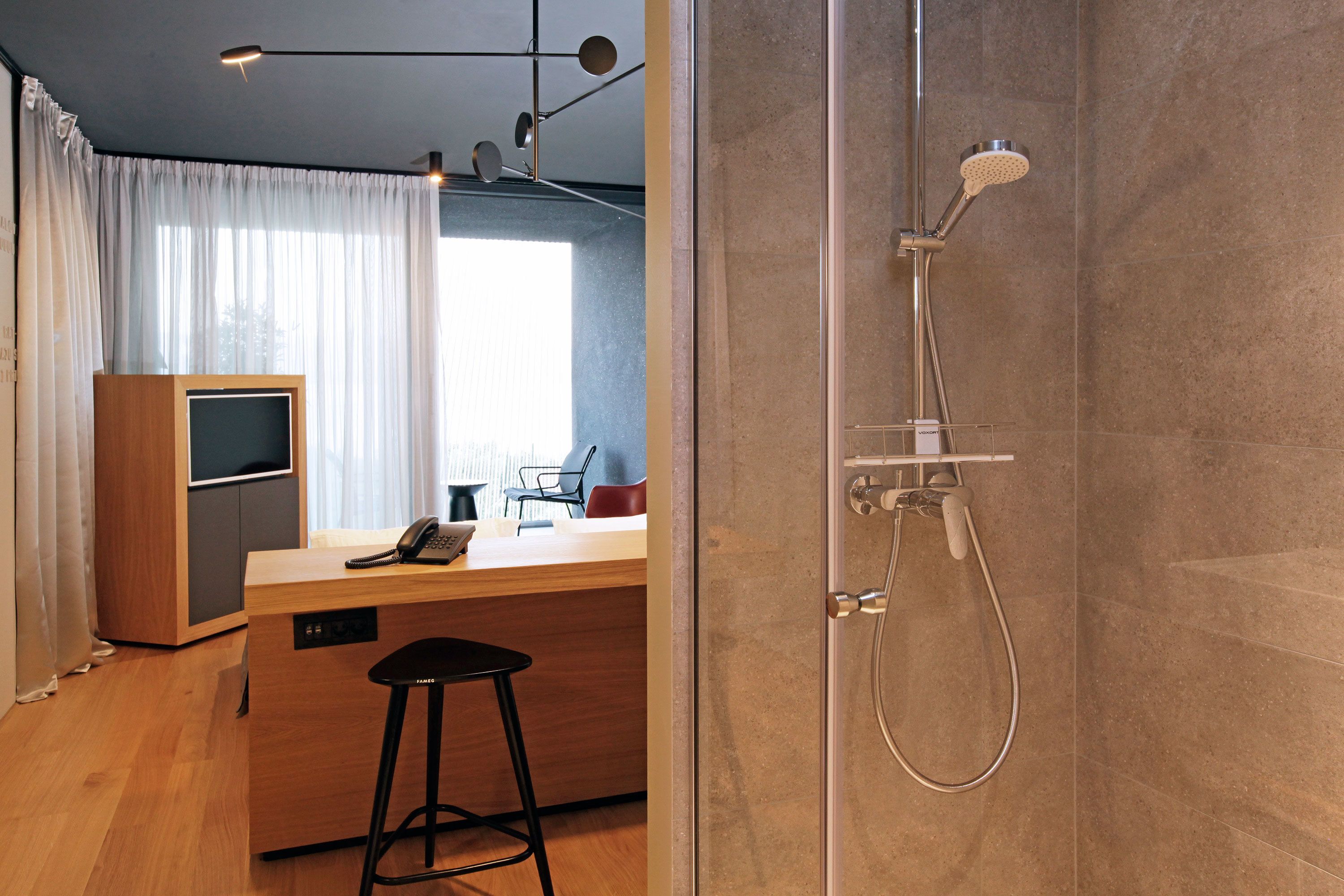Ein modernes Badezimmer mit einer gläsernen Duschkabine, einem Holztisch mit Telefon und einem Barhocker.