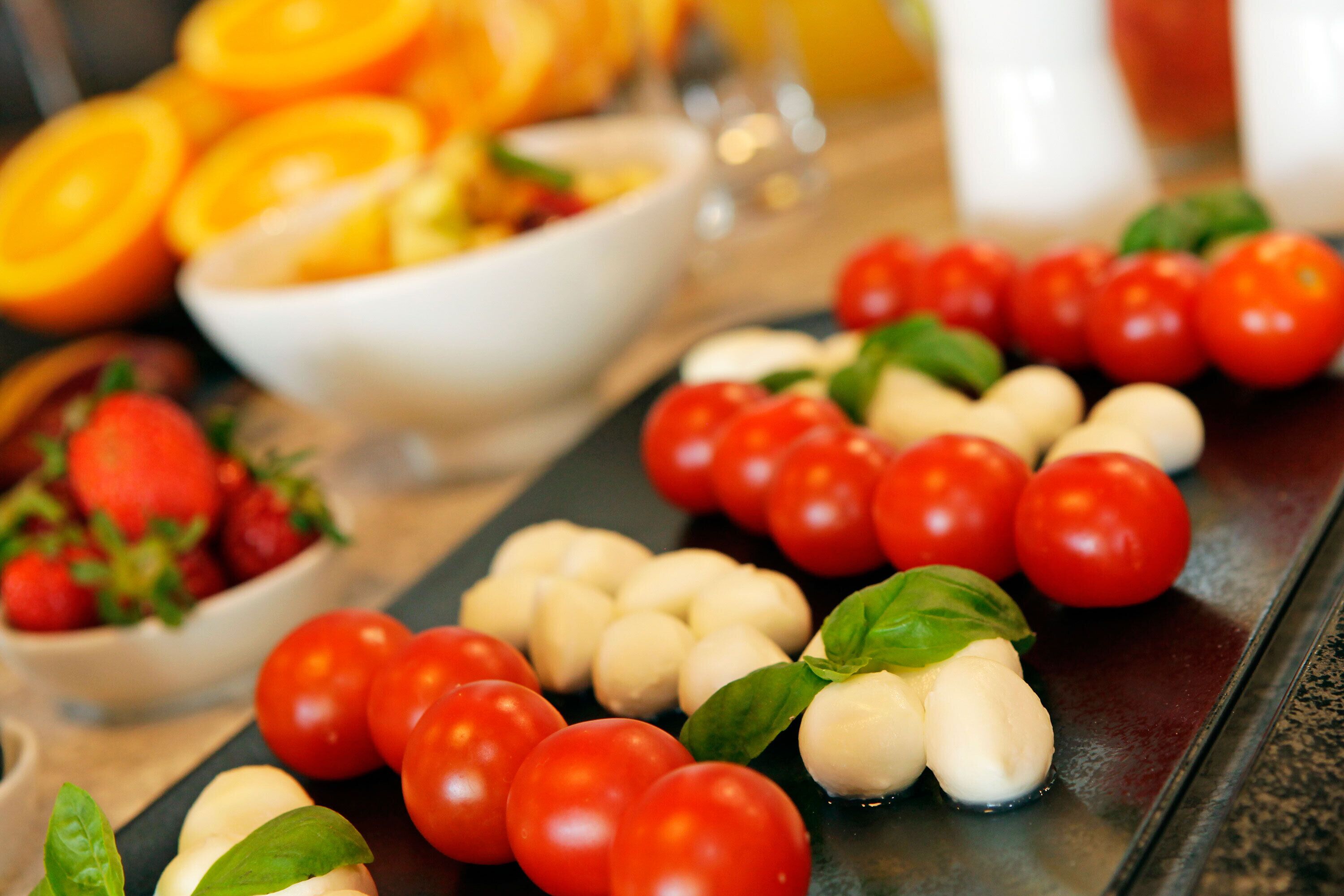 A table with tomatoes, mozzarella balls, and basil leaves.