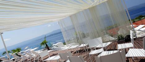 A terrace with white chairs and a white canopy overlooking the ocean.