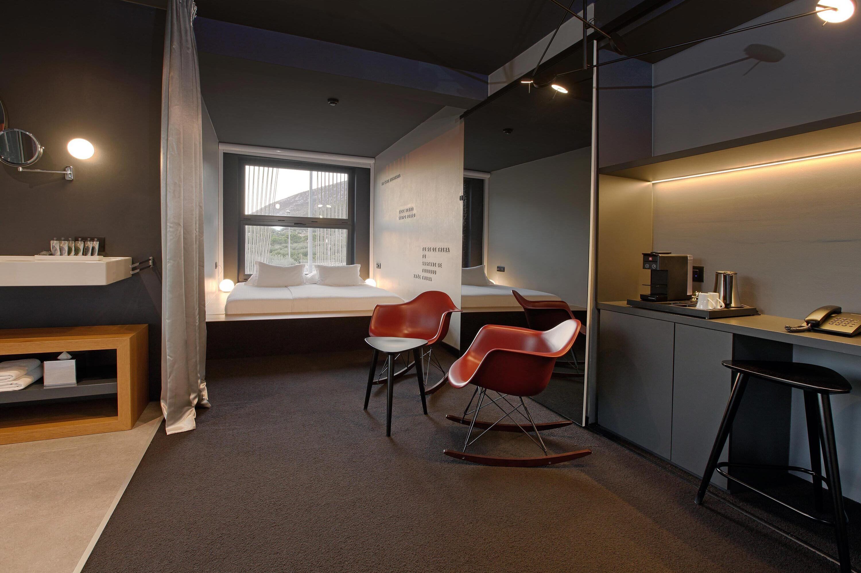 Une chambre d’hôtel moderne équipée d’un lit, d’un bureau avec un ordinateur, d’une chaise, d’une petite table et d’une étagère contenant des articles de toilette.