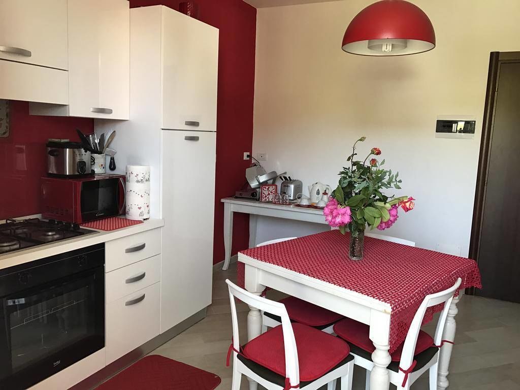 A kitchen with white cabinets, a red wall, a dining table with a red tablecloth, and a vase with flowers.